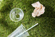 recycling, garbage disposal, environment and ecology concept - close up of used disposable plastic cup with straw and tissue on grass