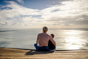 Wall Mural - Mother and 3 years old son hugging each other and enjoying the beautiful ocean views