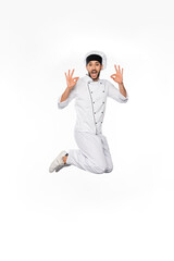 Wall Mural - excited chef in hat and uniform jumping and showing okay on white.