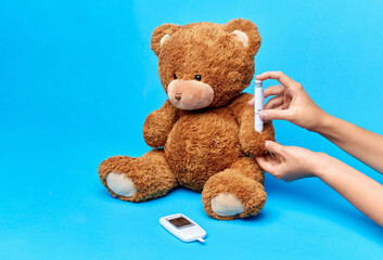 Wall Mural - medicine, healthcare and diabetes concept - hands with insulin pen making injection to teddy bear toy over blue background