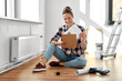 repair, people and real estate concept - woman with clipboard sitting on floor at home
