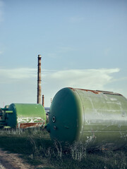 Used metal containers for industrial production lie on the grass, there is a cardboard production plant nearby