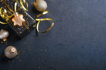 Wall Mural - Holiday gift box or present with ribbon, golden confetti and gold baubles on black background. Magic christmas greeting card. Christmas Decoration. Border design. Mock up. Top view.