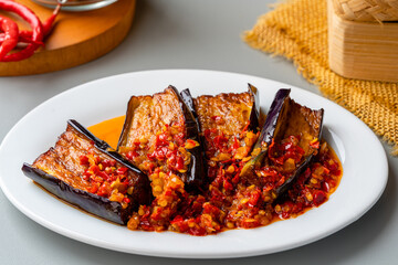 Wall Mural - Terong Balado or eggplant with sambal balado. Serving in white plate on gray background. Indonesian food and cuisine, authentic from Padang, West Sumatera.