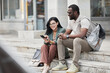 © Seventyfour - Portrait of two young business people chatting while sitting on steps in city, copy space