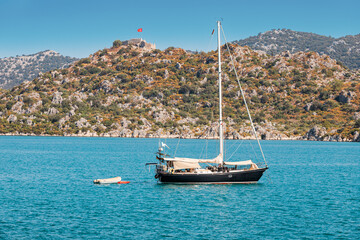 Poster - Cruise yacht sails on the sea near the sunken ancient town of Kekova in Turkey against the background of castle Simena on a high rock with Turkish flag