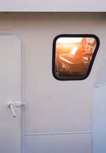 Part Of Metal Door With Blurred Flare Light Reflection On Porthole Surface Of Navigation Bridge Room In White Tugboat Ship