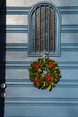 Decorative Advent wreath or crown with red berries bonded with holly or ilex branches and foliage and fixed at the window of a house entrance door with a fabric ribbon