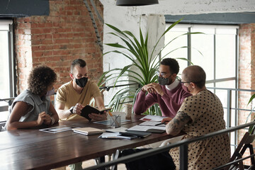 Aufkleber - Group of young colleagues in protective masks planning work and discussing new ideas at meeting while sitting by table