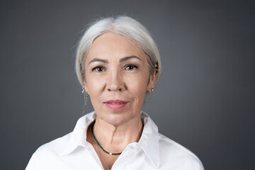 Portrait of senior woman with white hair in white blouse looking at camera isolated on grey background