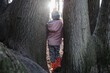 © Cavan Images - child standing between trees in a forest at sunset in winter