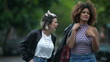 © Marco - Candid two diverse women walking together outside in street laughing and smiling