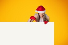 Christmas Happy Woman In Santa Hat Pointing At White Advertisement Board With Hand.
