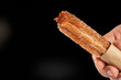 hand holding churro filled with dulce de leche on black background with copy space