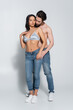 © LIGHTFIELD STUDIOS - full length view of shirtless man and sexy woman in bra standing in jeans on grey.