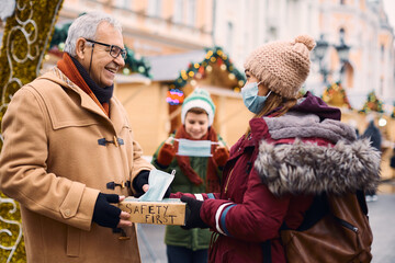 Canvas Print - Happy senior man takes face mask at Christmas market entrance checkpoint due to coronavirus pandemic.