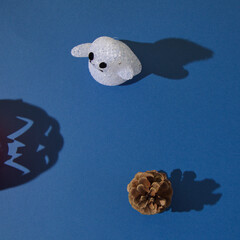 Poster - Ghost and a pine cone with shadows, with a shadow of halloween pumpkin on a blue background