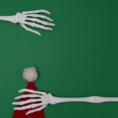 Sticker - Skeleton's hand holds Santa's hat. Green background with copy space