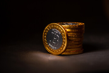 Sticker - Close up of a golden bitcoin leaning on a pile of coins on a black background, Stock Market Concept