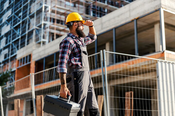 Wall Mural - A hardworking worker with a toolbox in hand is arriving at a construction site. He is looking at the site and, he is ready to do his job.