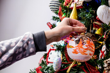 Sticker - Female hand hanging a Christmas decoration and ornament on the Christmas tree