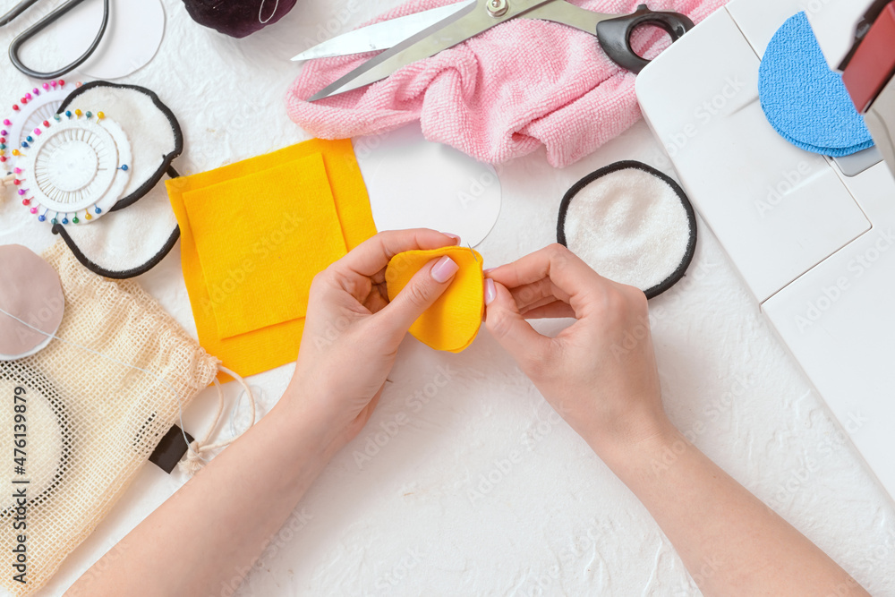 Woman with needle making reusable cotton pad on white background