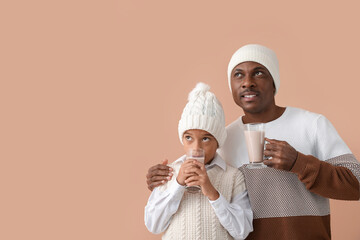 Poster - African-American boy and his father in winter clothes and with tasty hot chocolate on color background