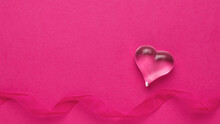 A Figure Of A Glass Heart And A Ribbon On A Pink Background. The Concept Of Valentine's Day.
