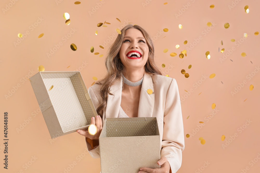 Beautiful young woman with gift and falling confetti on beige background