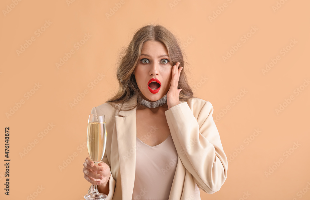 Surprised young woman with champagne on color background