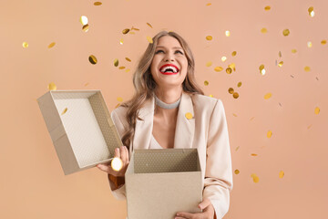 Wall Mural - Beautiful young woman with gift and falling confetti on beige background