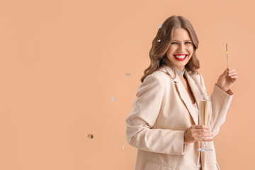 Sticker - Beautiful young woman with Christmas sparkler and champagne on beige background