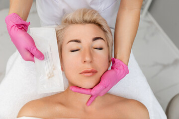 woman a cosmetology procedure of thread lifting. cosmetologist shows the needles for the procedure. 