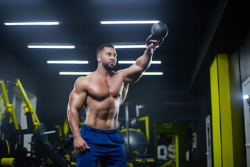 Portrait of a muscular sportsman performing kettlebell swings with one hand in a gym