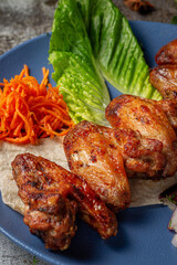 Canvas Print - Serving a dish from the restaurant menu. Chicken wings, grilled nuggets with grated carrots and herbs on a plate against a gray stone table, delicious kebab