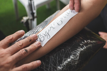 A professional tattoo artist places a stencil of a tattoo design unto the moistened skin of a client's forearm.