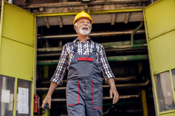 Wall Mural - A happy senior factory worker exiting the factory and holding a walkie-talkie in his hands. A factory worker at the factory.