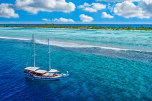 Small Yacht Sailing In Tropical Sea Over Coral Reef In Indian Ocean Lagoon. Exotic Island Landscape, Aerial View, Stunning Nature Scenic. Amazing Vacation Destination, Coastline, Waves, Sunny Sky