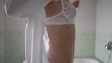Young Woman In Lace Lingerie Putting On White Shirt In Slow Motion Turning. Portrait Of Confident Slim Caucasian Smiling Lady Getting Dressed In Bathroom In The Morning. Seduction And Erotics