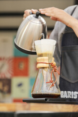 Vertical shot of a barista pouring water in a pour-over style coffeemaker on a food weight scale