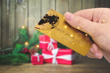 Sticker - Young woman holding a credit card and a gift box against the background of Christmas decor, shopping on the Internet,