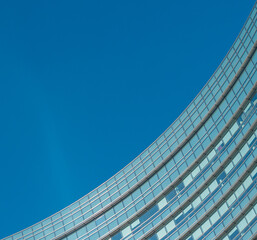 Symmetrical  curve detail of a blue glass windows work office building, with blue sky in the back. 