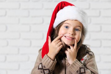 Canvas Print - Little cute beautiful girl in red Santa hat smiling and looking into the camera.