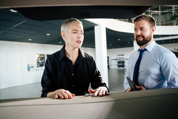 Canvas Print - An attentive female buyer and male seller are studying the details in the open trunk of the car