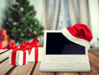 Wall Mural - Laptop computer standing on the table with a gift and Santa hat in a cozy room