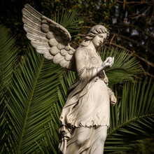White Angel Statue With Tropical Trees On The Background In The Park