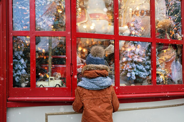 Wall Mural - boy watching festive window display at gift store.  New Year and Christmas holidays concept. Child and christmas shop window. winter season