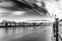 Long Exposure In Black And White Of Downtown Maastricht With A View On The Silky Water Of The Meuse River And A Dramatic Sky Full Of Clouds In Motion.