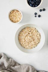 Wall Mural - Bowl of porridge, bowl of blueberries and a bowl of oats on white marble countertop