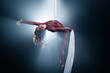 Curly female gymnast performs on a black background with rays. circus artist on white aerial silks